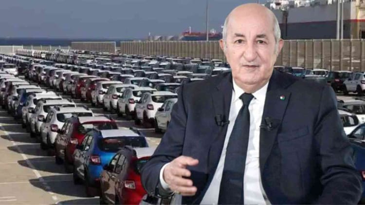 Homme en costume devant un grand parking de voitures neuves.