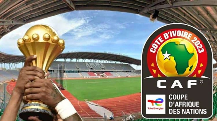 Etre humain tenant le trophée de la CAN 2023 à Lomé, stade vide en arrière-plan.