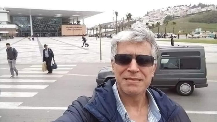Homme portant lunettes de soleil devant un bâtiment moderne.