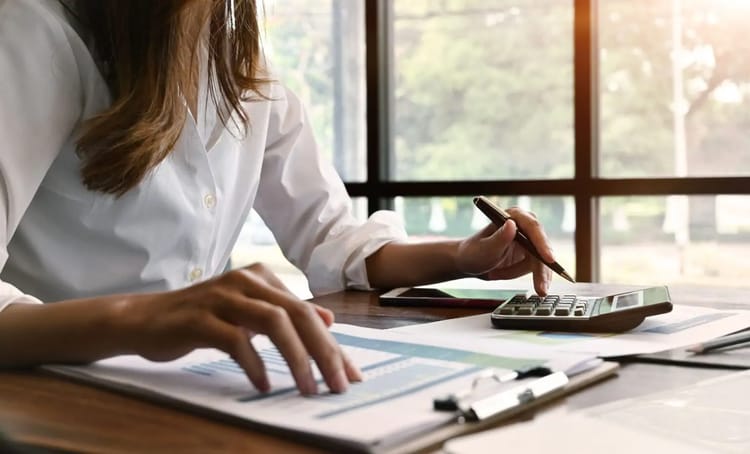 Femme utilisant une calculatrice et un smartphone pour gérer ses finances.