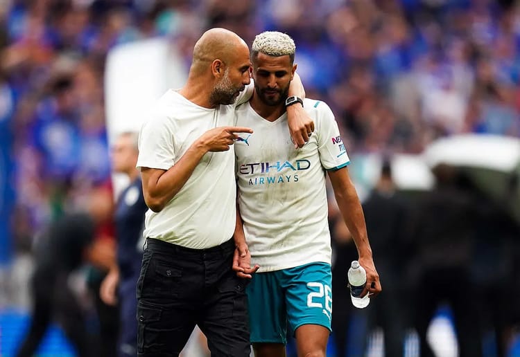 Mahrez et l'entraîneur discutant sur le terrain de football.