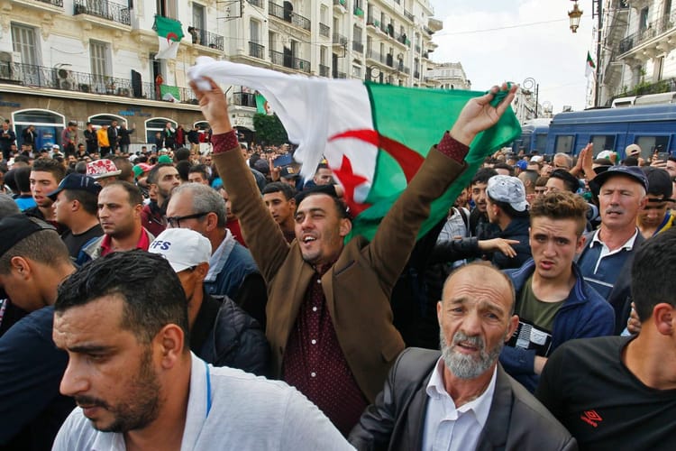 Algérie : colère grandissante des Algériens face à la gouvernance - Des chiffres révélés malgré la censure Manifestants algériens dans une rue, certains brandissant un drapeau national.