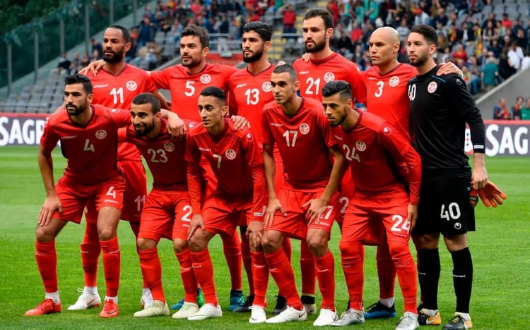 Groupe de joueurs tunisiens en tenue rouge sur le terrain de football.