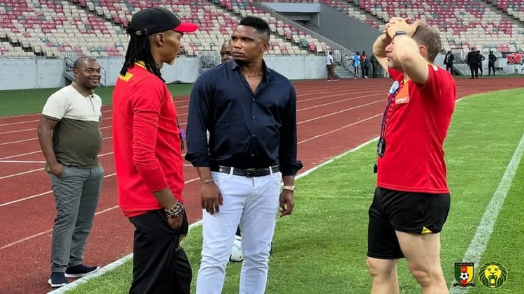 Fin de parcours pour Rigobert Song : Eto’o lui réserve une mauvaise surprise Trois hommes discutent sur le terrain de football en tenue sportive et décontractée.