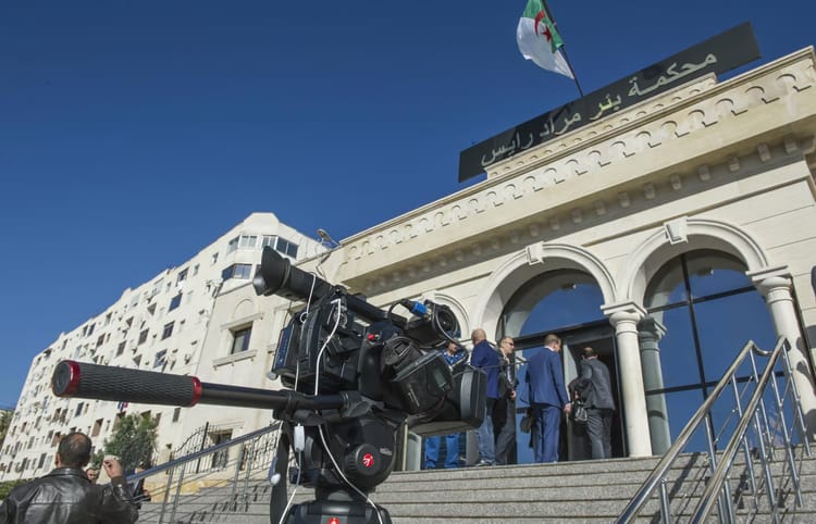 Caméra de presse devant un tribunal en Algérie, justice en cours.