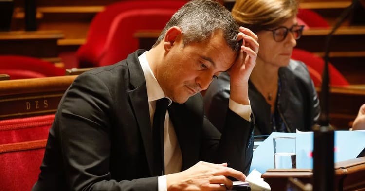 Homme en costume noir, assis, semble stressé ou concentré en séance parlementaire.