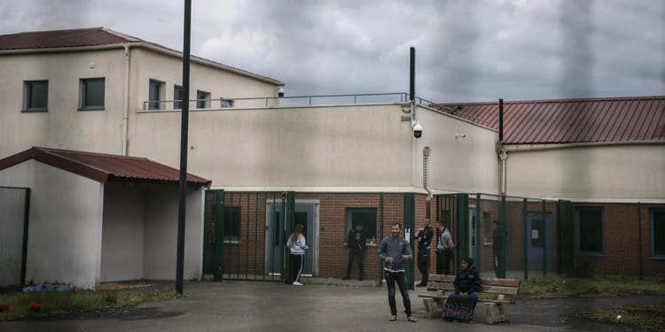 Groupe de personnes en rétention, surveillées par des agents de sécurité.