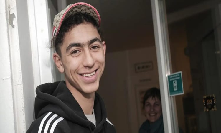 Jeune adolescent algérien souriant, sauveur de vie, à la porte d'une maison.