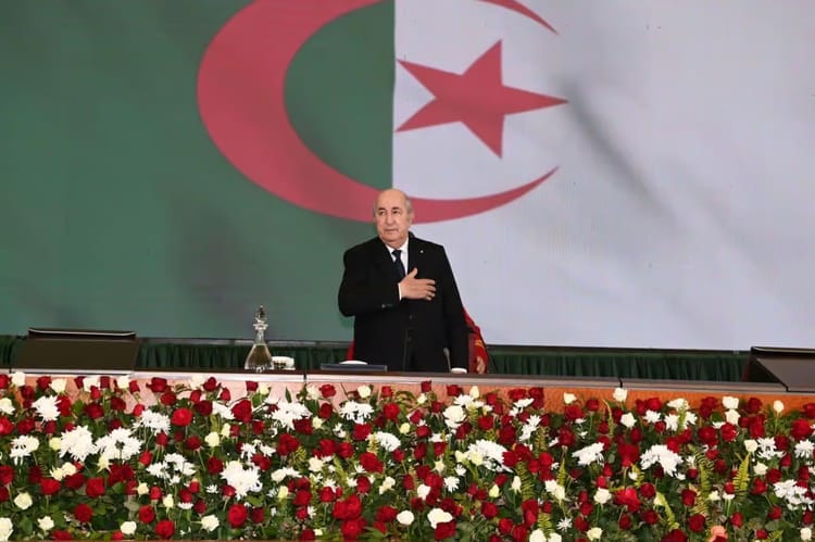 Président Tebboune lors d'un discours avec drapeau algérien en arrière-plan.