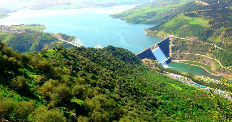 Le barrage de Béni Haroun, rempli après de fortes pluies, entouré de verdure et de montagnes.