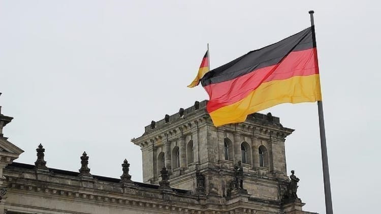 Opportunité en Allemagne : Programme de Bourses AFRIKA KOMMT! pour les Algériens Drapeau allemand flottant devant un bâtiment historique en Allemagne.