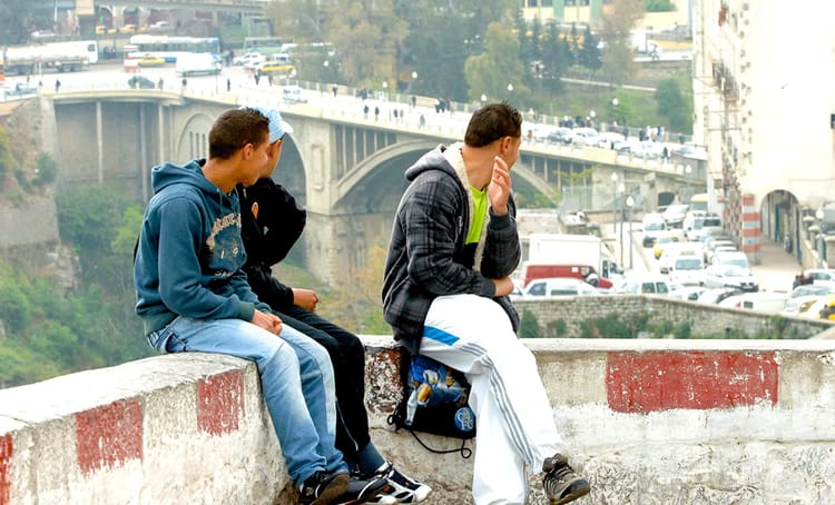 Jeunes hommes assis sur un mur avec un pont en arrière-plan à Alger.