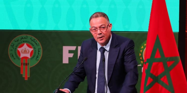 Maroc : Fouzi Lekjaa brave la CAF et annonce les dates potentielles de la CAN 2025 ! Fouzi Lekjaa parle lors d'une conférence avec drapeau marocain en arrière-plan.