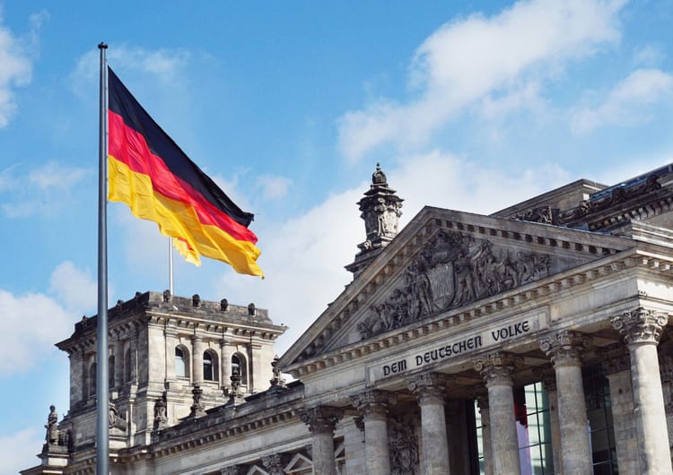 L'Allemagne Ouvre ses Portes aux Travailleurs Qualifiés : Ce que Vous Devez Savoir Drapeau allemand flottant devant un bâtiment historique en Allemagne.