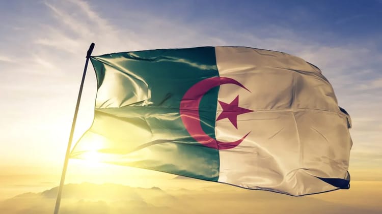 Drapeau algérien flottant au vent avec coucher de soleil en arrière-plan.