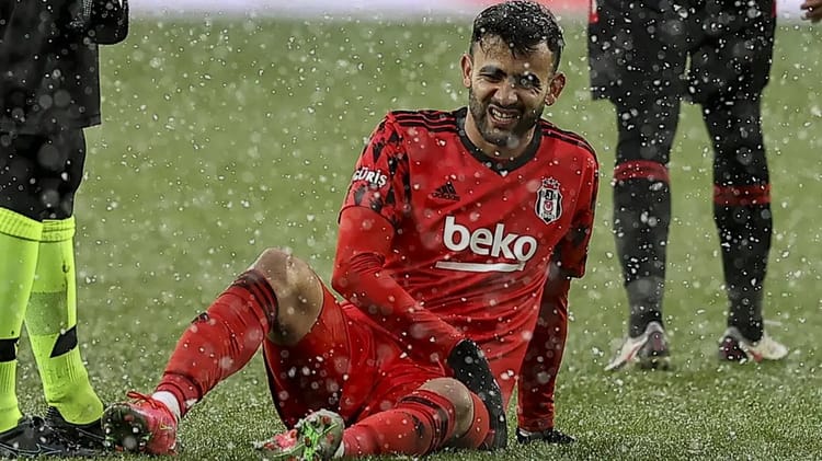Rachid Ghezzal en tenue de football, blessé sur le terrain sous la pluie.