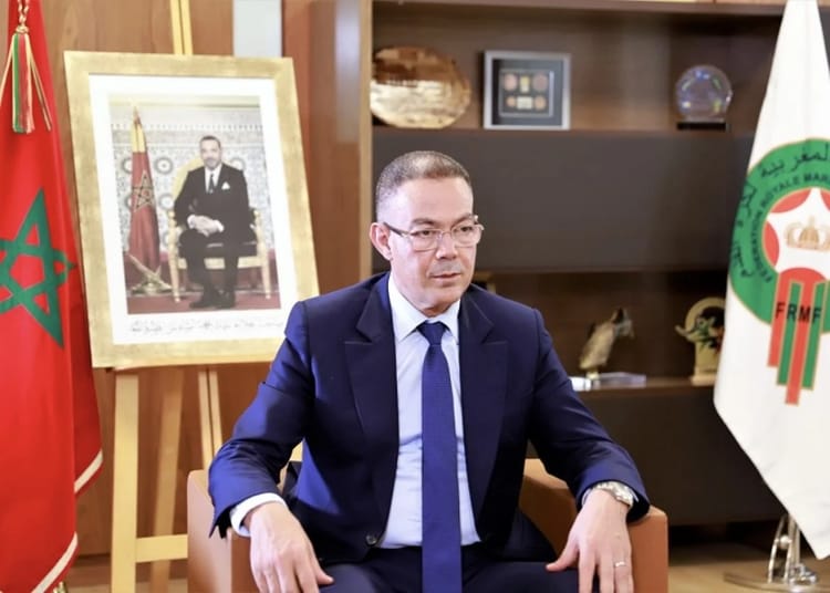 Le Maroc, co-organisateur du mondial 2030 : Fouzi Lekjaa démontre une fois encore à la face du monde, son charisme Fouzi Lekjaa en costume dans un bureau avec drapeaux marocains.