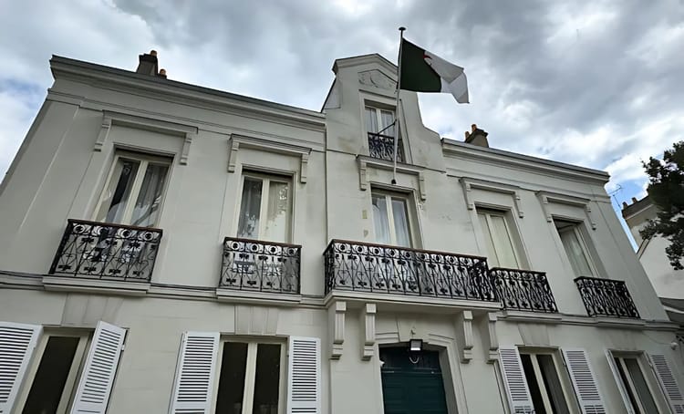 Bâtiment blanc avec drapeau français en haut, ciel nuageux.