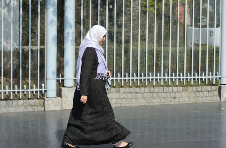 Femme en hijab marchant près d'une clôture en métal en France.
