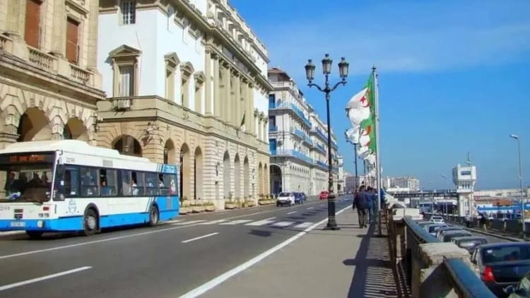 Promenade en bord de mer à Alger avec bus et bâtiments historiques.