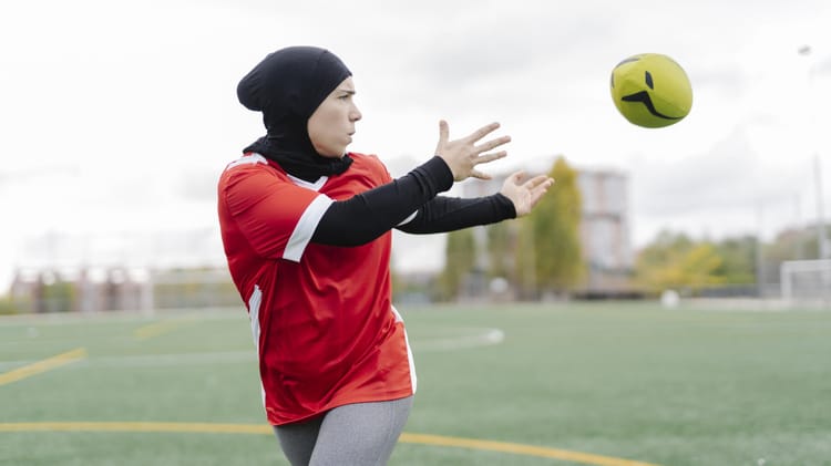 Femme musulmane en hijab jouant au football sur un terrain.
