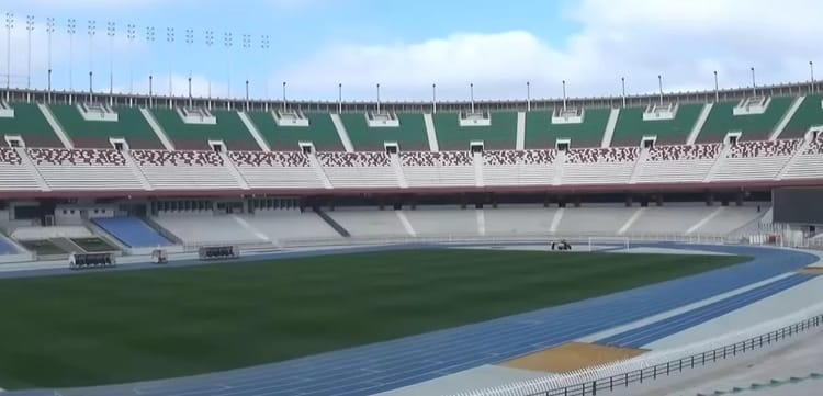 Stade 5 Juillet avec pelouse endommagée et tribunes vides.