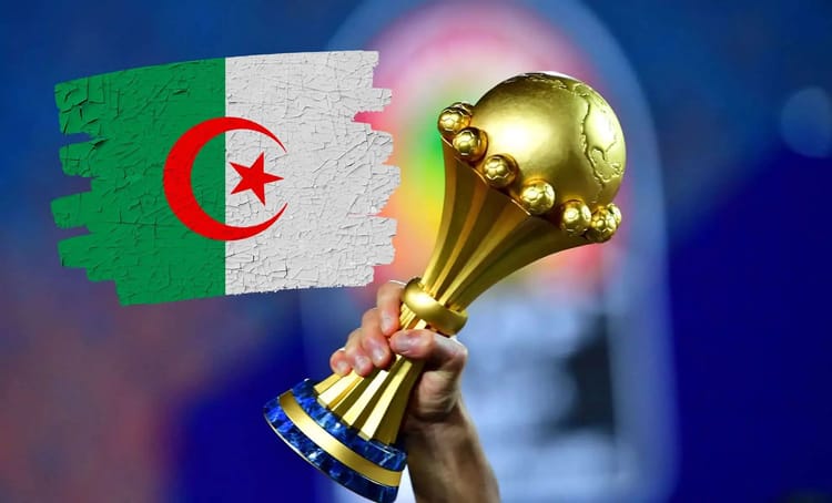 CHAN 2025 : L’Algérie pourrait revenir sur sa décision Main tenant une coupe de football avec drapeau algérien en arrière-plan.