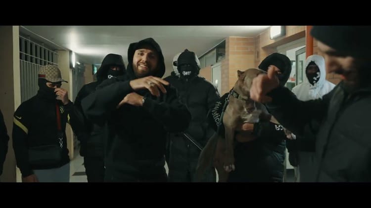 Groupe de jeunes hommes en tenue sombre, certains masqués, dans un couloir urbain.