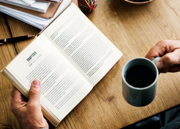 Trump pivots hard away from fight against unvanquished pandemic Personne lisant un livre avec une tasse de café sur un bureau en bois.