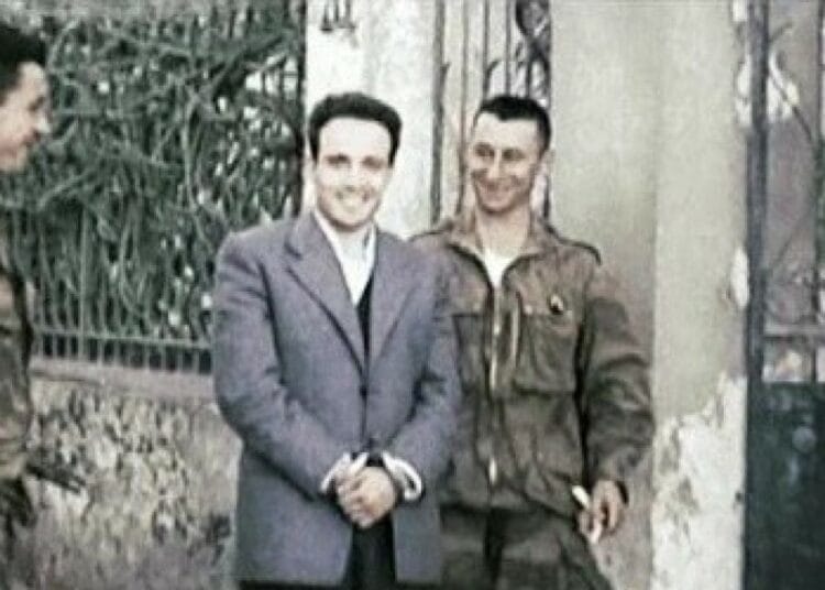 Assassinat de Larbi Ben M’hidi : Emmanuel Macron rompt 67 ans de silence et reconnaît le crime d'État Deux hommes en costume et uniforme se serrent la main devant une grille en fer forgé.