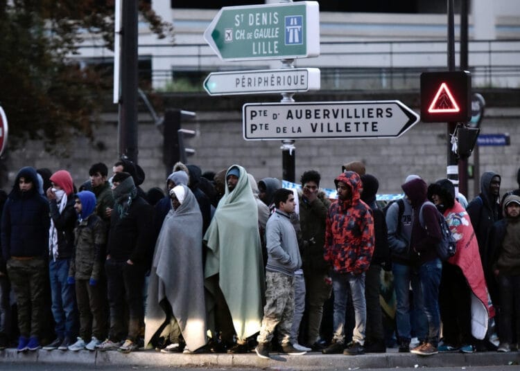 Groupe de migrants en attente à Lille, France, sous un panneau de signalisation.