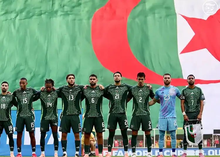Les joueurs de l'équipe d'Algérie alignés devant un drapeau national.