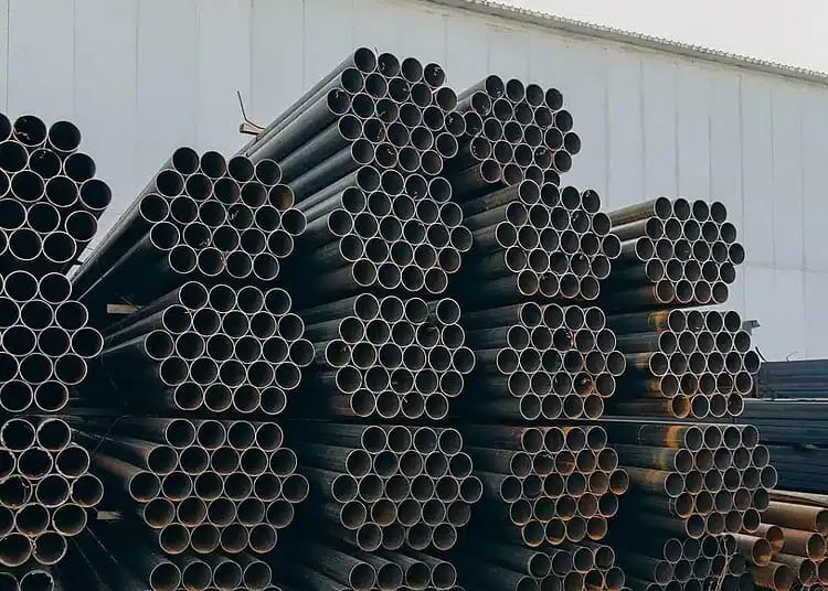 Tuyaux en acier noirs empilés dans une usine de fabrication.