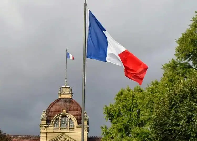 Drapeau français sur un mât avec ciel nuageux en arrière-plan.