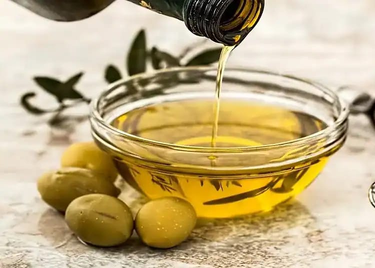 Top 4 des huiles d’olive algériennes plébiscitées en 2024 Huile d'olive versée dans un bol avec olives vertes.