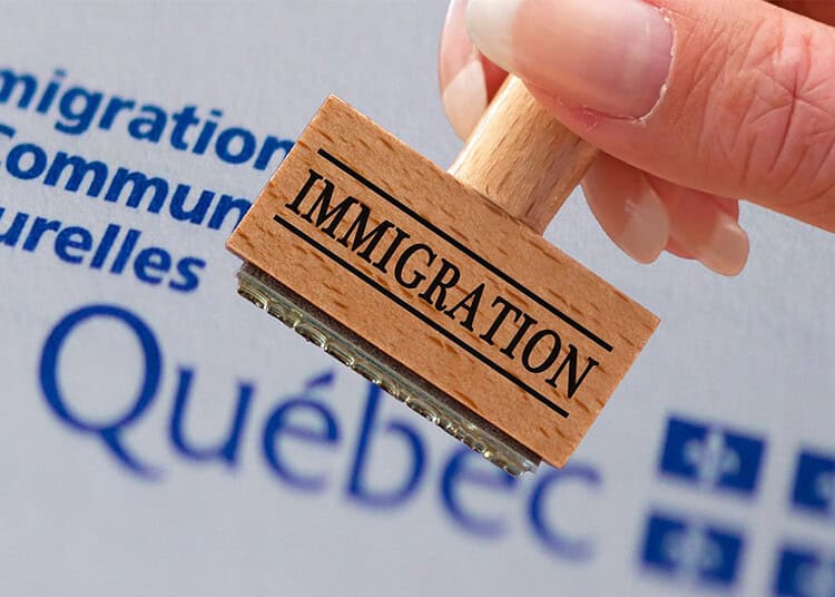 Québec : les expulsions de Maghrébins explosent en 2025 Tampon en bois avec le mot 'Immigration' devant un logo du Québec.