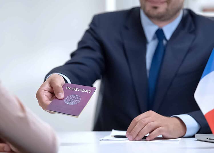 Titres de séjour en France : une préfecture change ses règles Homme en costume avec passeport et drapeau français sur le bureau.