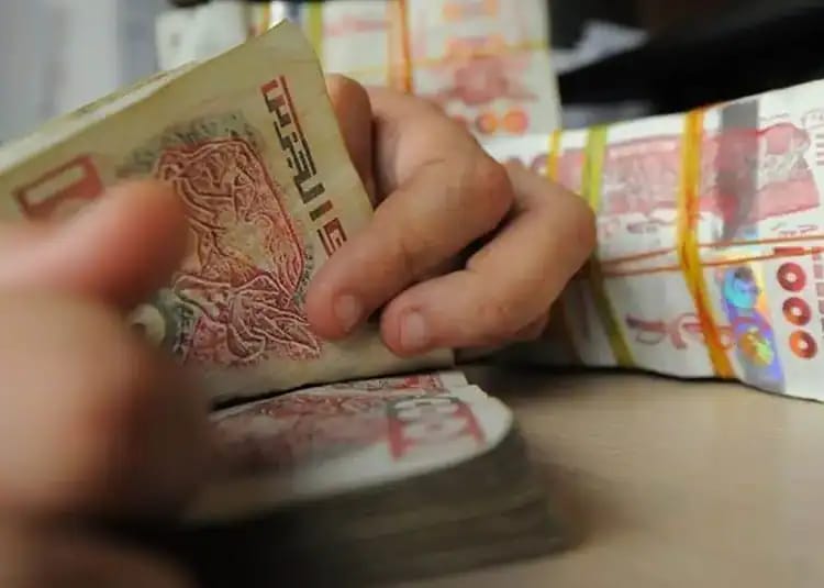Dinar algérien : euro et dollar, écart record ce 30 mai 2026 Main manipulant des billets de banque algériens en rouleaux.