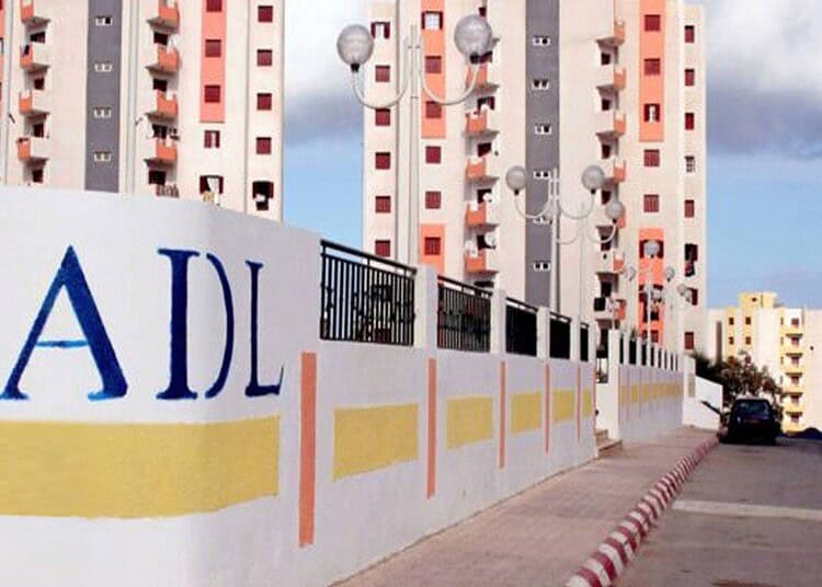 AADL 3 : nouveau délai de 30 jours pour payer la 1ère tranche Mur de livraison AADL 3 avec logo visible, bâtiments en arrière-plan.