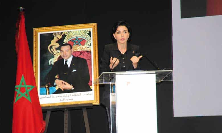 Rachida Dati parlant lors d'une conférence avec portrait du roi du Maroc en arrière-plan.