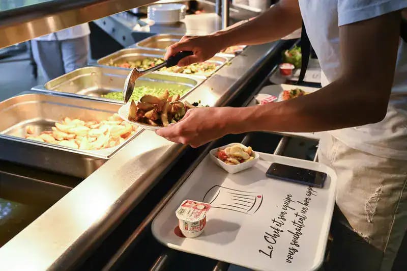 Étudiant servant un repas dans une cafétéria universitaire en France.